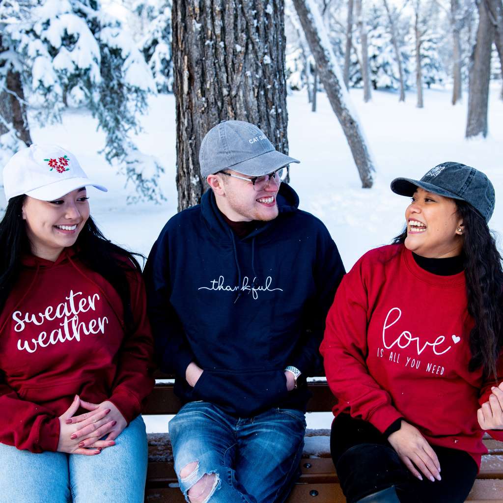 Friends sitting in winter embroidered sweatshirts that say sweater weather, thankful and love is all you need - DSY Lifestyle