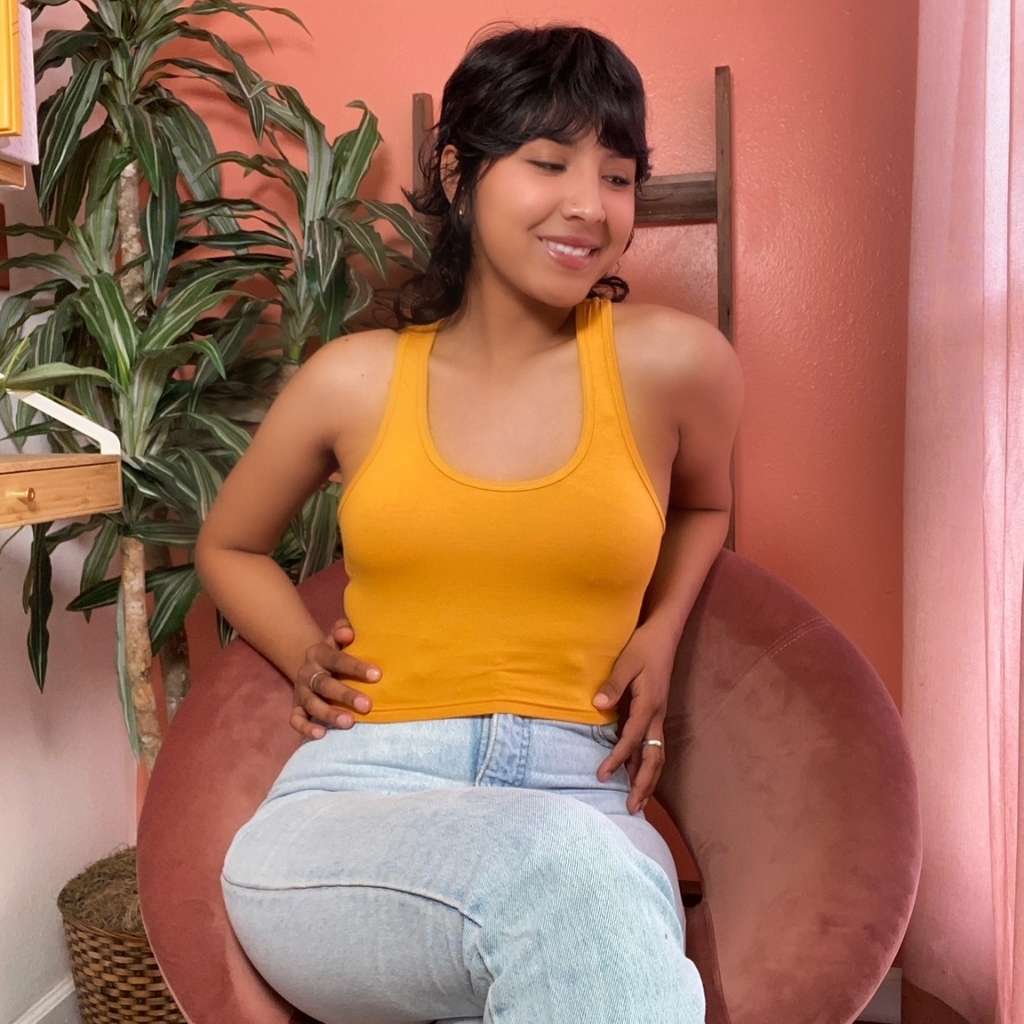 female sitting in a chair with a mustard color Racerback crop tank top and denim jeans-DSY Lifestyle