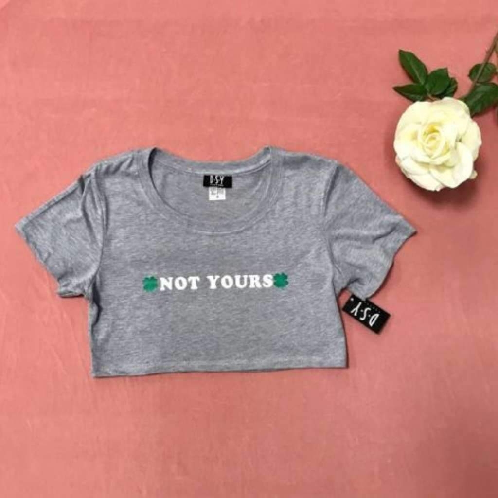 Flat lay of heather grey crop top with not yours printed on the front paired with jean shorts and sneakers - DSY Lifestyle